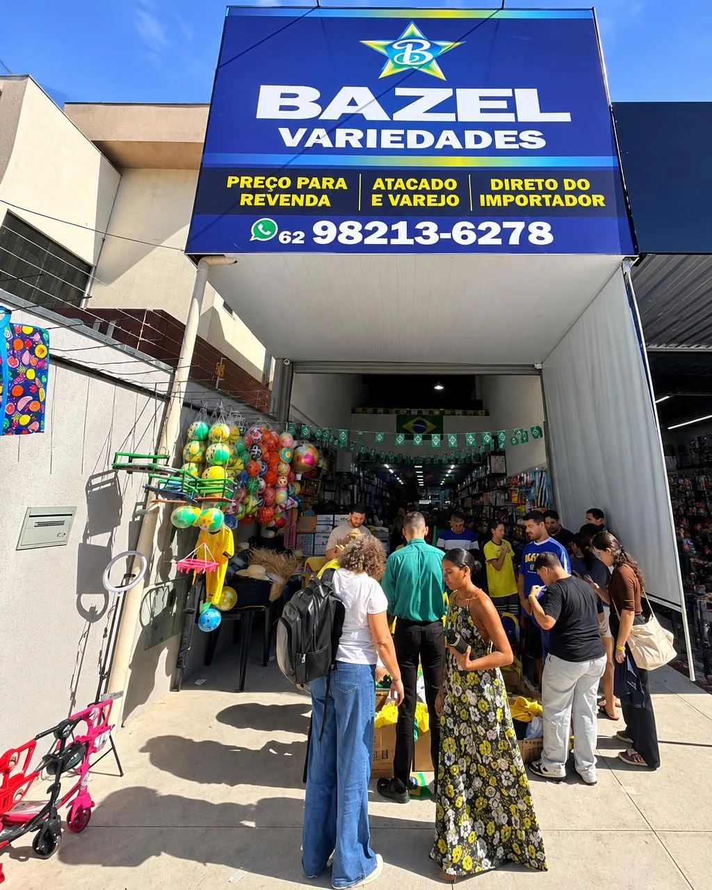 Fachada da Bazel Variedades com clientes na entrada e a placa azul da loja